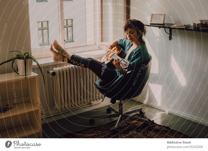 Content woman playing guitar at home content relaxed casual barefoot acoustic minimalistic room floor sit musician guitarist crossed legs young adult leisure