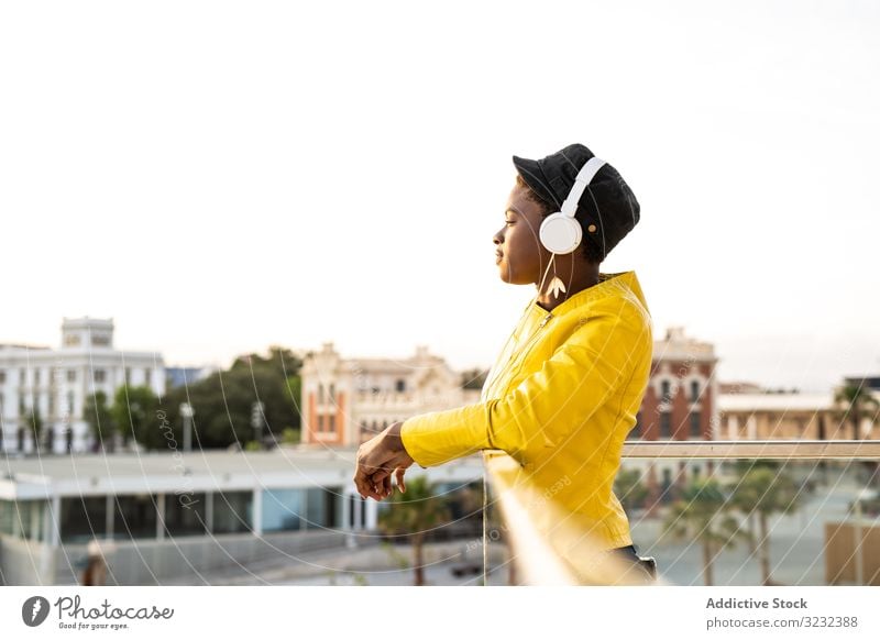 Peaceful female enjoying music and relaxing on balcony woman headphones peaceful content trendy african american lean glass jacket listen happy sound young