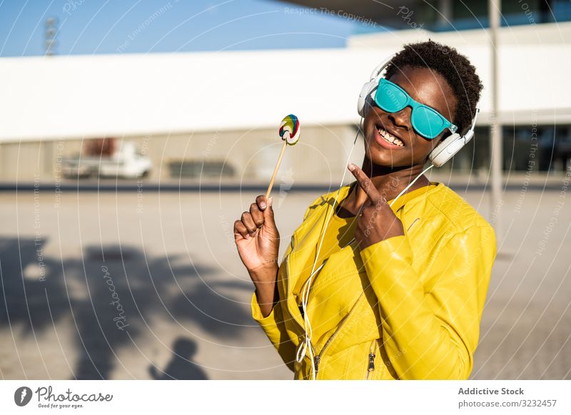 Black woman eating candy lollipop cool trendy african american female jacket yellow sunglasses enjoy sweet summer fun stick young fashion cute relax chill