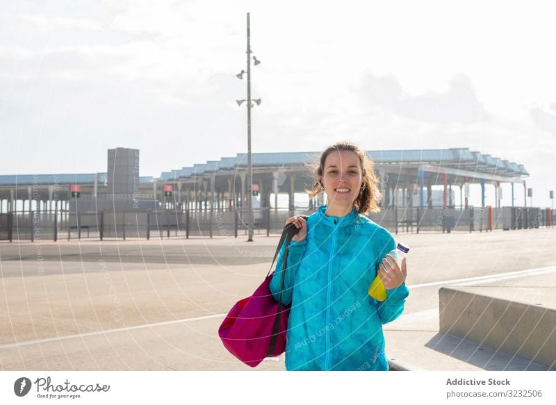 Smiling sportswoman holding bag and bottle while standing outdoor street walking city leisure style outdoors urban activity athlete athletic body carry