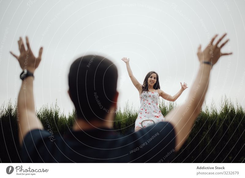 Joyful couple on playground against grassy field excited seesaw fun happy town romantic casual green bonding rest valley relaxed swings greeting hands up young