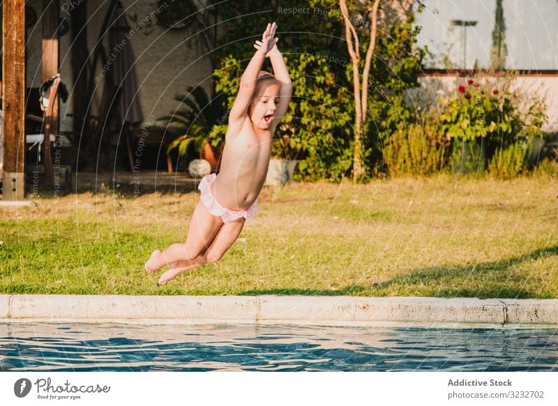 Cheerful girl jumping into pool water scream raised arms fun yard play kid child little hands up panties shirtless garden vacation weekend summer joy happy