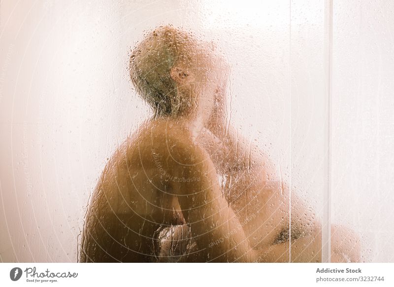 Woman behind wet glass in shower woman transparent partition bathroom water drop young female care body clean clear hygiene sensual translucent skincare routine