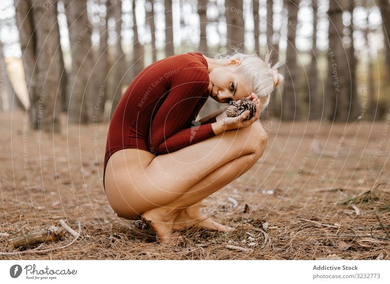 Beautiful modern woman resting barefoot in evergreen forest woods harmony squatting primitive embracing knees blonde carefree attractive beautiful charming