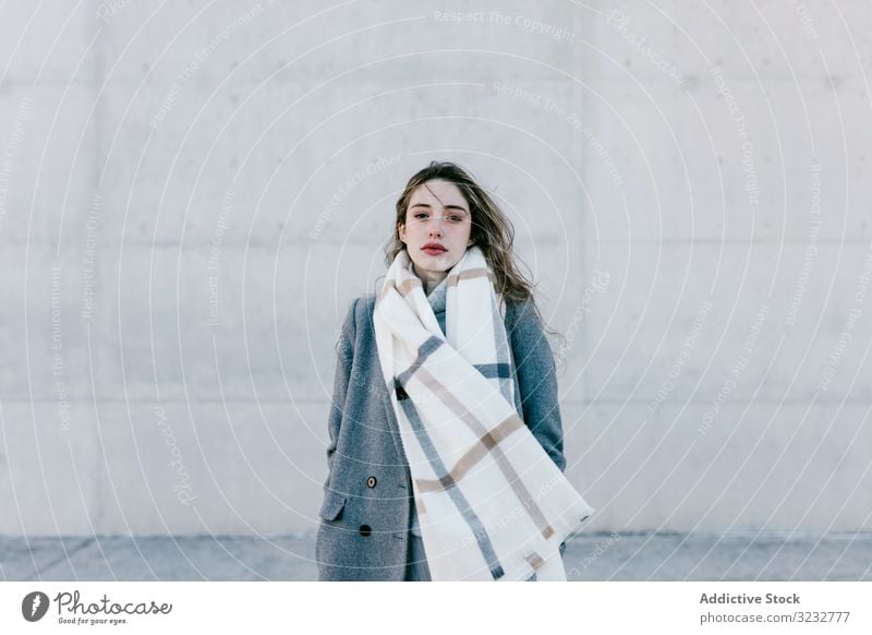 Young woman in coat and scarf on windy day stylish street wall city building female urban fashion cool young model outfit warm weather exterior lady long hair