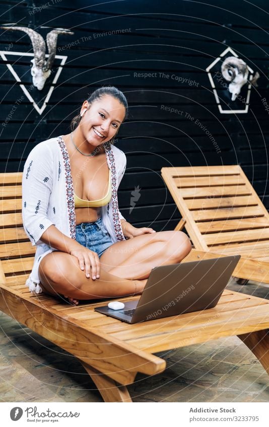 Relaxed woman using laptop while resting on deck chair relaxed browsing cheerful smile wooden terrace tropical sit casual crossed legs costa rica young adult