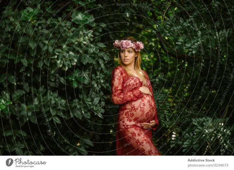 Pregnant woman with closed eyes touching belly and chin while standing in garden in sunny day pregnant expectation prenatal maternity dream forest childbearing