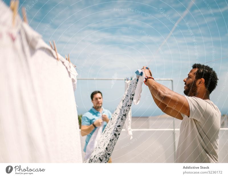 Multiracial men hanging clothes in bright day housekeeping laundering understanding fashion laundry housework homework linen relationship together support