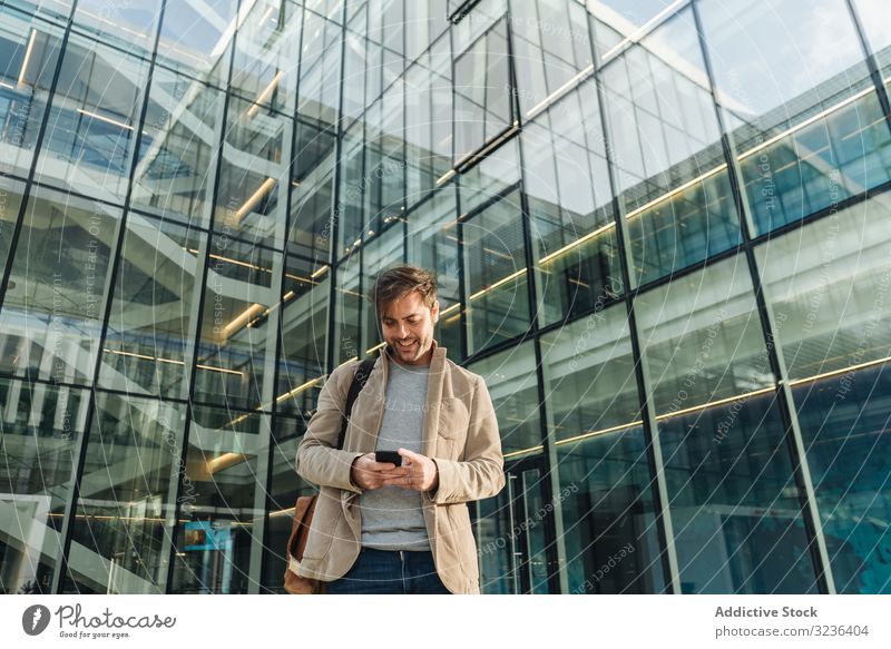 Smiling entrepreneur using smartphone outside office building businessman street city positive modern smile adult center hand in pocket male elegant casual