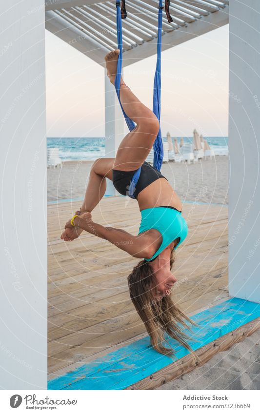 Relaxed woman performing aerial yoga hanging head down and touching leg hanging down exercise balance acrobatic fitness anti-gravity yoga young posture training