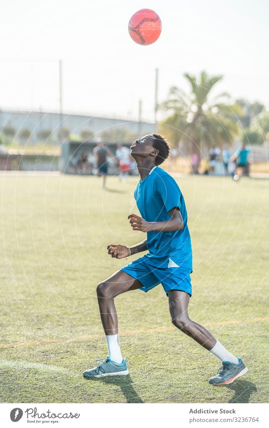 Skinny black teenager jugging football ball on head juggle field training player sportswear ethnic grass male adolescent soccer lawn sunny daytime