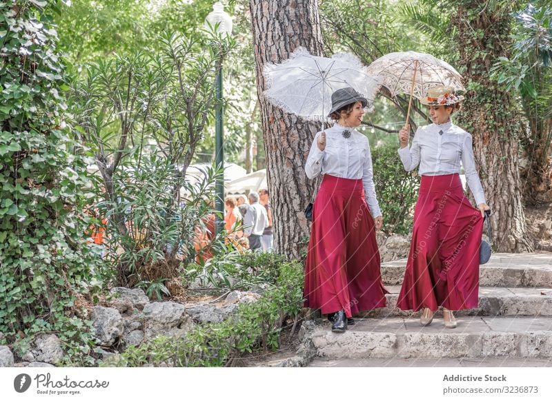 Vintage women walking in park together talk vintage step dress parasol smile costume female summer event retro old fashioned umbrella cheerful happy friend