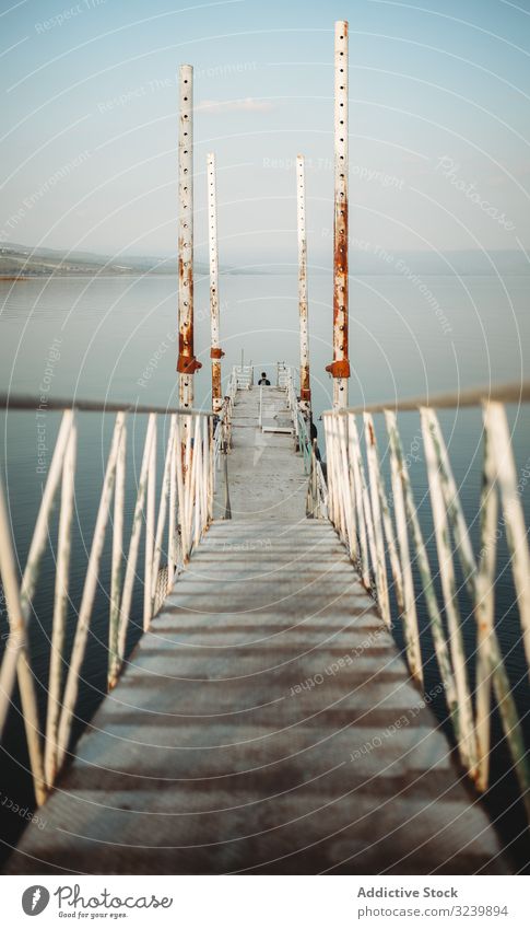 Rusty pier near calm sea water rusty narrow railing sky cloudless weathered traveler evening structure construction path way shabby rough ocean tranquil serene