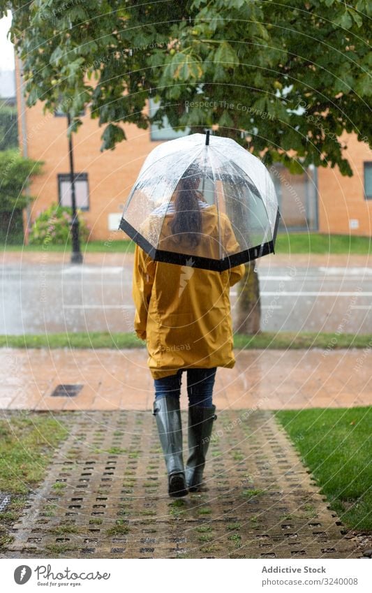 Woman in yellow raincoat and rubber boots with umbrella under rain woman street wet road puddle autumn walking season weather environment october protection