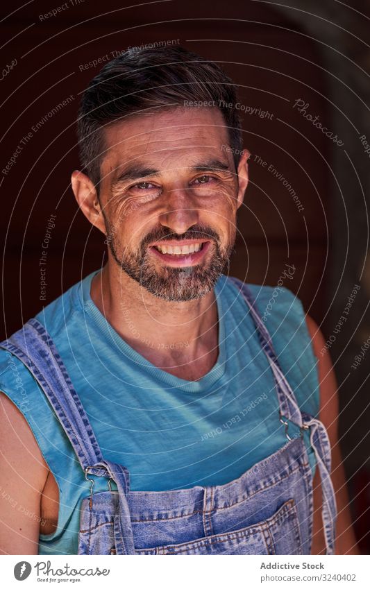 Smiling workman in denim overall looking at camera portrait craftsman worker overalls happy smile middle aged beard cheerful service male professional mechanic