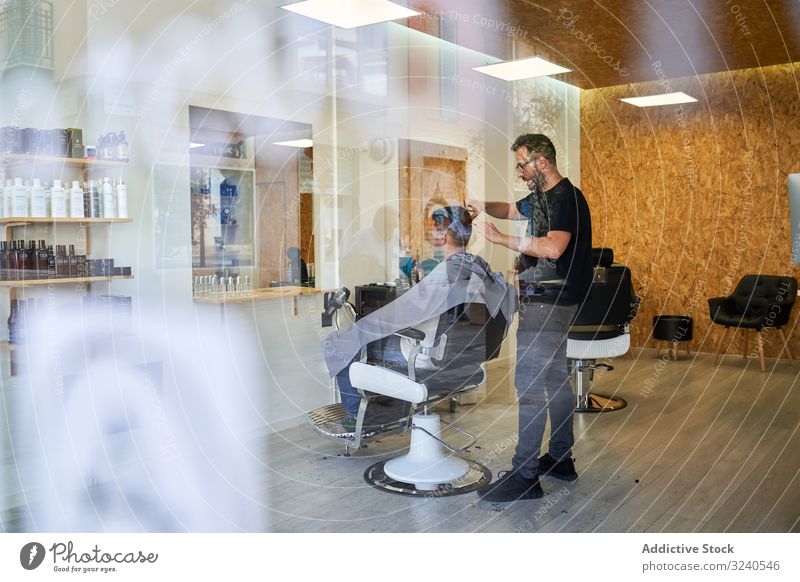 Barber shop from outside through fogged glass with a barber inside cutting a client's hair vertical reflexion window storefront street outdoors shaver