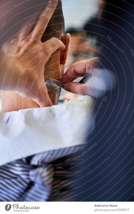 Vertical photo of a detail of a barber's hands cutting a client's hair with a razor vertical handmade vintage nape service mirror reflexion shaver barbershop