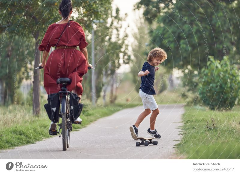 Mother and son riding along park path mother ride skateboard bicycle together fun family happy boy woman child kid summer joy glad pleasure smile cheerful