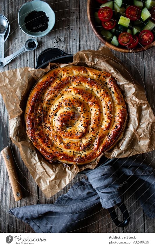 From above crop cook holding hot baking dish with fresh puff pastry and serving piece of borek on plateFaceless person serving homemade borek on wooden table