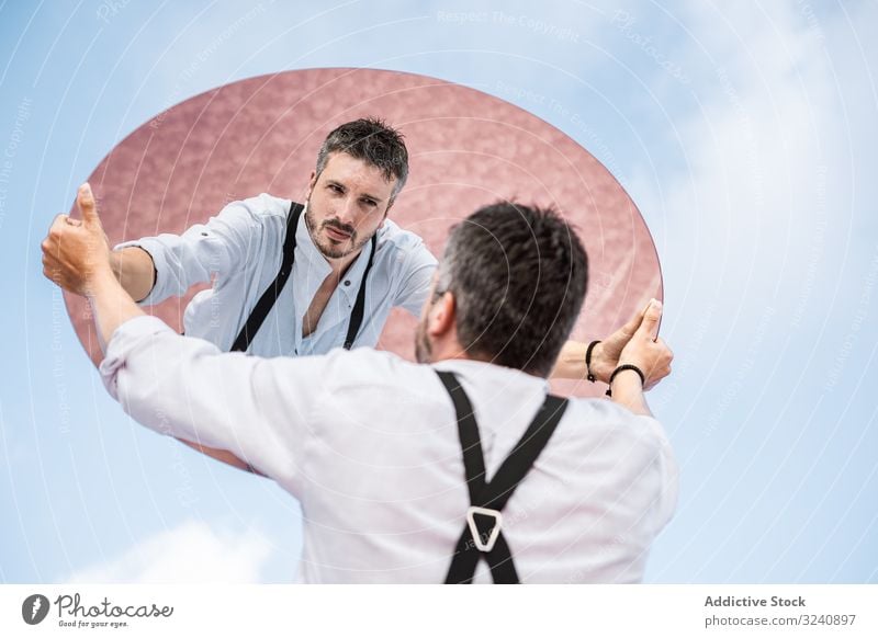 Stylish man holding mirror up and reflecting reflection stylish pensive white shirt suspenders stand blue sky lifting carrying handsome oval surreal usa concept