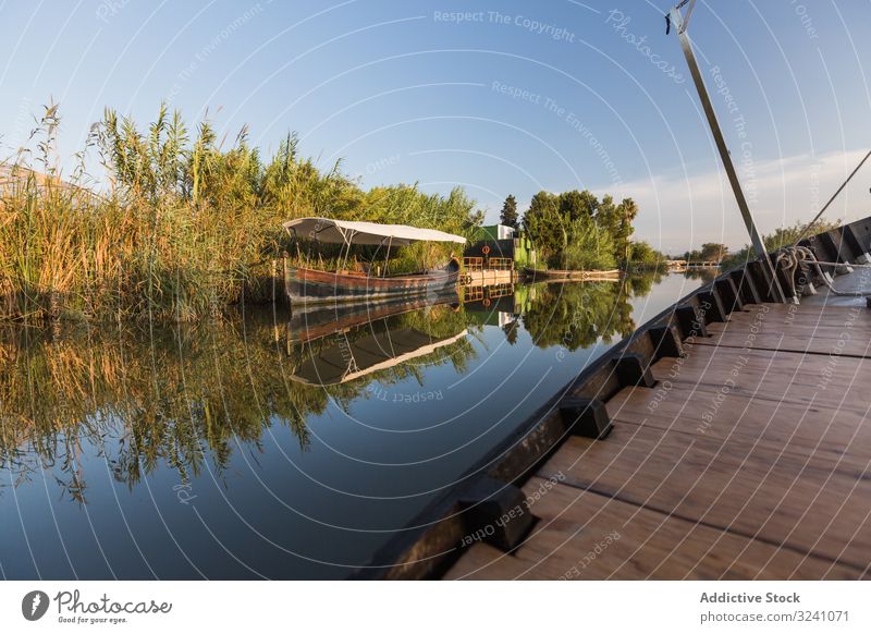 Side of modern boat sailing along rural shore vessel ride tranquil sunny coast lagoon valencia reflection smooth waterfront greenery side detail wooden new