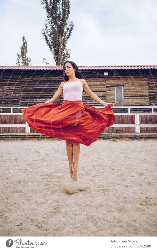 Woman in colorful skirt dancing at rural paddock woman dance red artistic jump sand enclosure barn farm daylight young adult culture dancer fun joy carefree