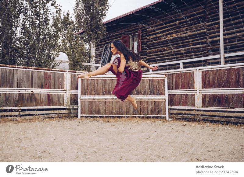 Expressive woman in colorful skirt dancing at rural paddock dance sheer artistic jump leg up sand enclosure barn farm daylight young adult culture dancer fun