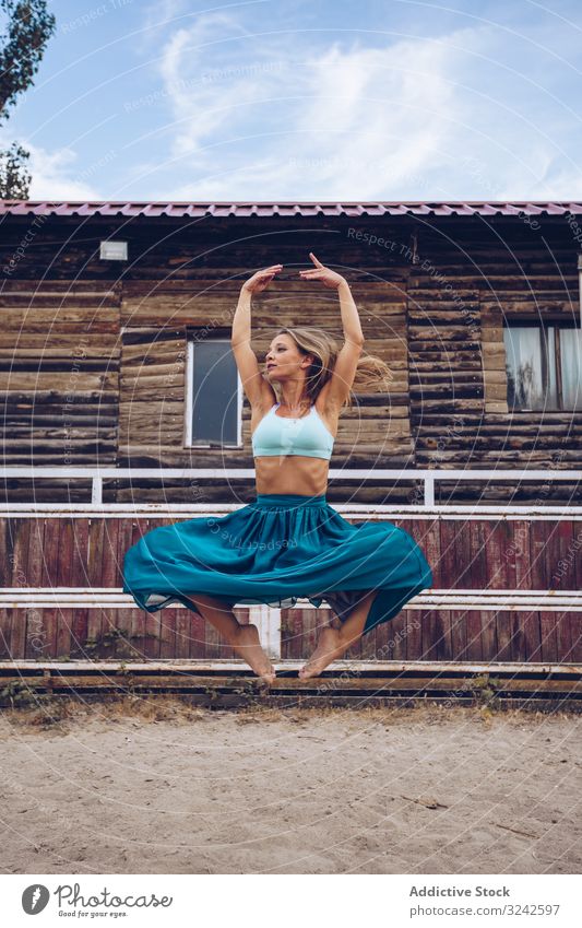 Flexible woman in colorful skirt dancing at rural paddock dance artistic jump sand bending flexible balance long enclosure barn farm daylight young adult