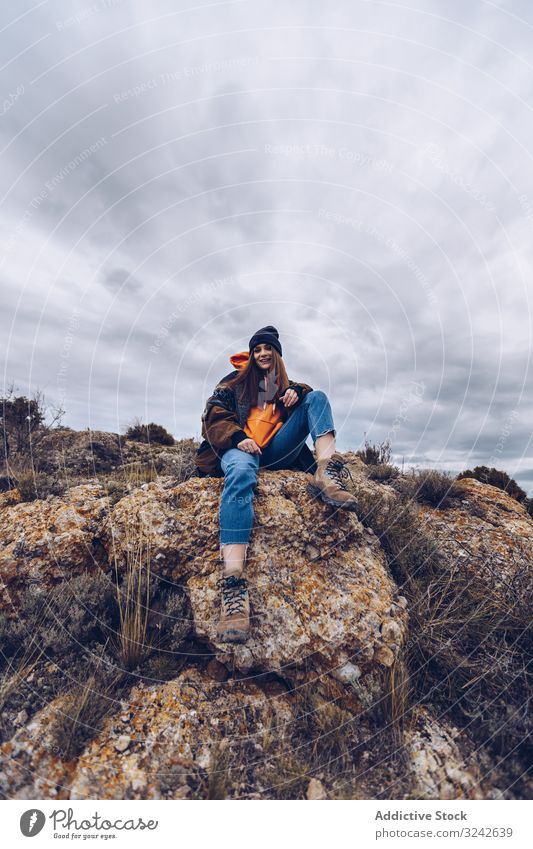 Cheerful woman resting on mountain top positive cheerful smile casual rock edge cliff picturesque young adult nature lifestyle attractive hiking travel healthy