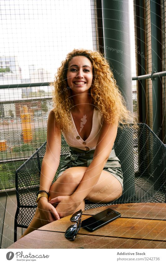 Smiling woman sitting in designed metal chair with sunglasses in hand lounge smartphone hall chill waiting area airport mobile vacation smile curly zone texas