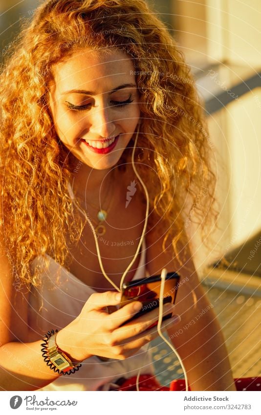 Smiling woman sitting on metal bench with earphones and smartphone music airport listen waiting area female casual style texas using selfie relax modern rest