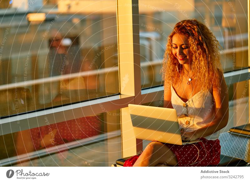 Enthusiastic woman working on laptop sitting on bench in airport hall travel typing using flight casual browsing backpack texas freelance gate remote journey