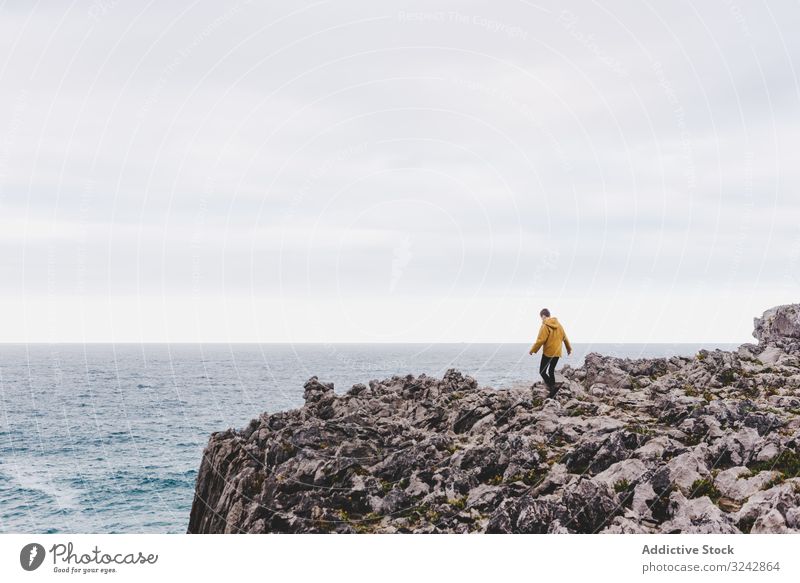 Traveler in solitude walking on rocky shore traveler seaside explore stone wanderlust contemplation lonely sweatshirt ocean hood water coast wave gloomy splash