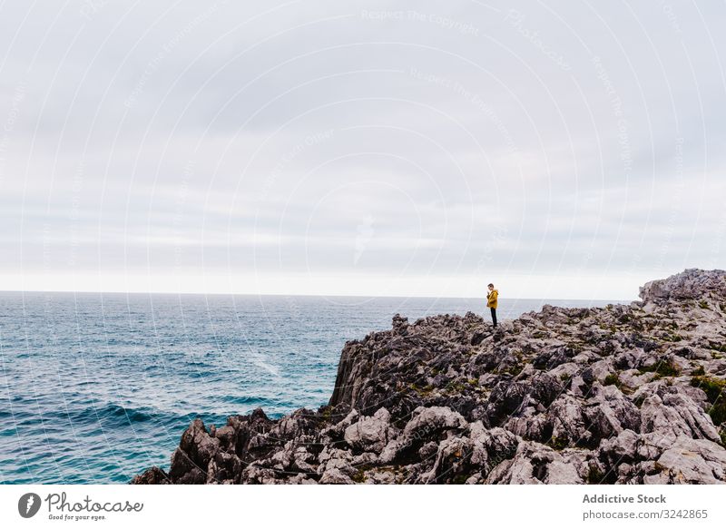 Traveler in solitude walking on rocky shore traveler seaside explore stone wanderlust contemplation lonely sweatshirt ocean hood water coast wave gloomy splash