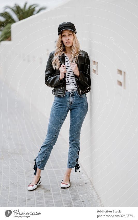 Stylish woman confidently leaning on white wall stylish cool urban trendy leather jacket provocative denim curly female lifestyle casual long haired modern