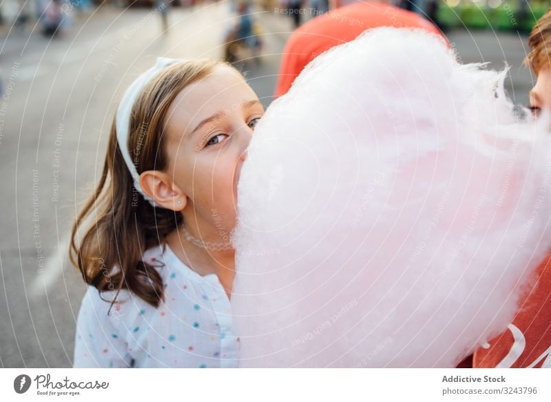 Cheerful girl eating cotton candy on street candyfloss stall smile city fair joy kid happy child urban town sweet fun vendor buy sell sidewalk pavement casual