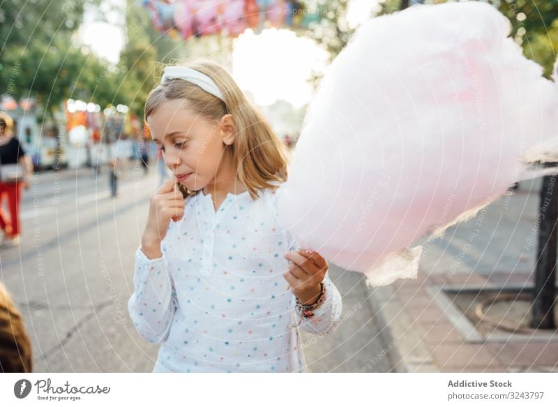 Cheerful girl eating cotton candy on street candyfloss stall smile city fair joy kid happy child urban town sweet fun vendor buy sell sidewalk pavement casual