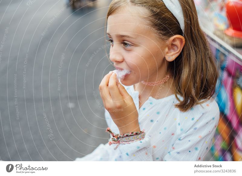 Cheerful girl eating cotton candy on street candyfloss stall smile city fair joy kid happy child urban town sweet fun vendor buy sell sidewalk pavement casual