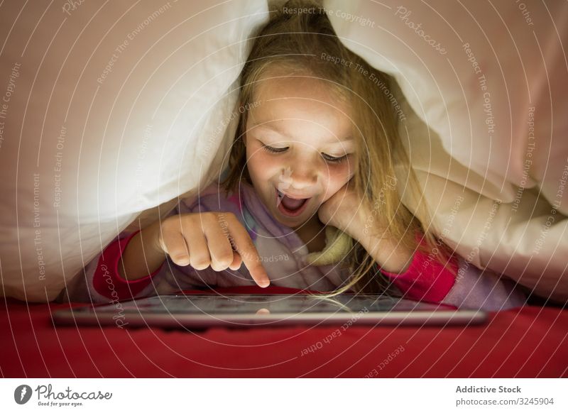 Girl using tablet under blanket girl bed hide watching playing bedtime pajama lying child happy fun positive enjoy red white kid preschooler cute little