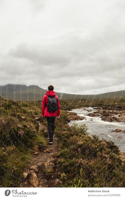 Tourist hiking along stream in meadow against mountain in clouds tourism trail water river adventure footpath trip travel environment person range wilderness