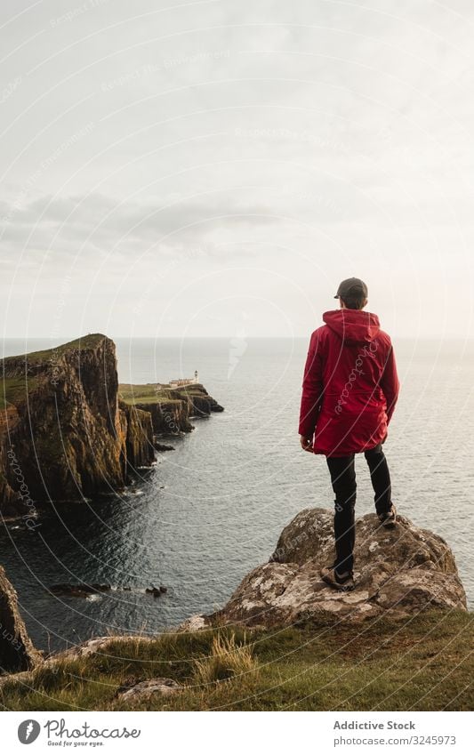 Lonely tourist standing on rocky coast against tranquil sea water under gray sky cliff adventure height viewpoint highland trip fresh wanderlust freedom woman