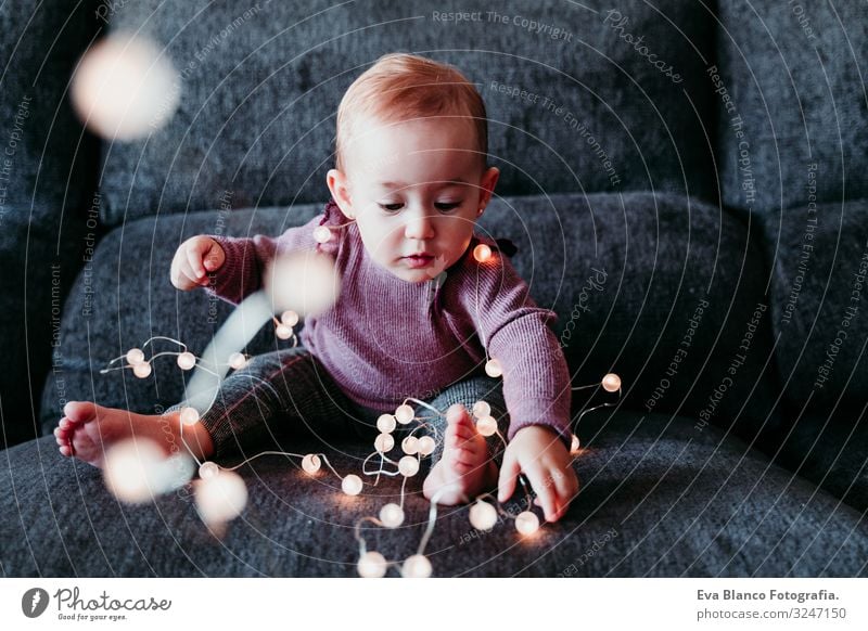 portrait of beautiful baby girl at home sitting on the sofa playing with a garland of lights Lifestyle Joy Leisure and hobbies Playing Flat (apartment)