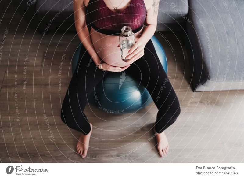 young pregnant woman at home sitting on pilates ball, drinking water. healthy lifestyle Pregnant Woman Yoga Home Sports Healthy Lifestyle Youth (Young adults)