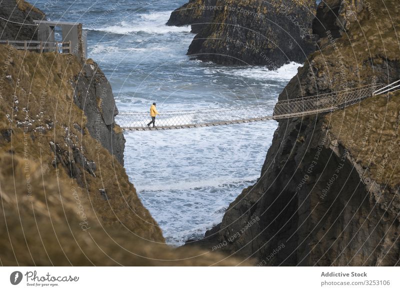 Tourist walking on rope bridge suspended between cliffs in Northern Ireland rock sea tourist ocean northern ireland person cross coast shore water landscape