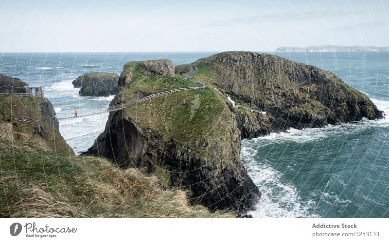 Tourist walking on rope bridge suspended between cliffs in Northern Ireland rock sea tourist ocean northern ireland person cross coast shore water landscape