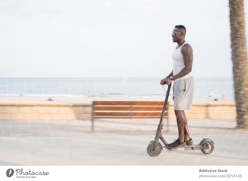 Cool adult black man riding scooter in street ride african ethnic electric scooter trendy cool fun drive promenade entertainment summer freedom transport male