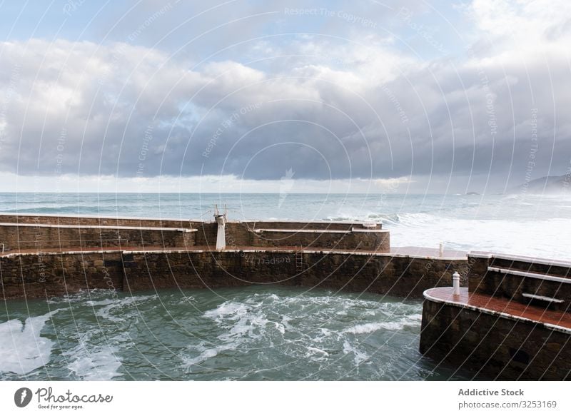 Rock breakwater with raging sea on cloudy weather landscape sky power fence wall foam wave surf tropical beach majestic ocean nature summer blue shore paradise