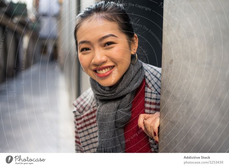 Joyful Asian resting female in casual clothing looking out modern wall of building at city street woman travel town tourist door peer peek playful exploring fun