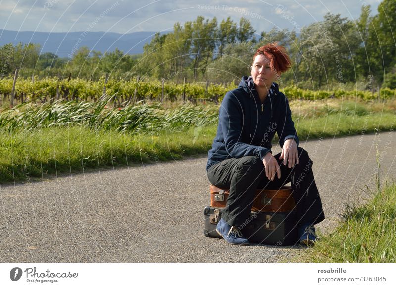 Middle-aged woman sits waiting on packed suitcases on a narrow country road in the countryside with wind Vacation & Travel Woman Adults 1 Human being