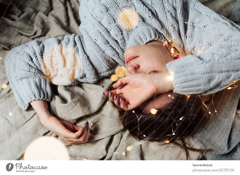 Young white woman lying in bed with fairy Christmas lights and bokeh around, shallow selective focus Bed Bedclothes Blur Caucasian Christmas & Advent